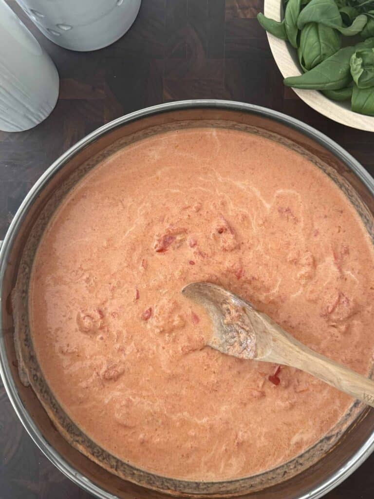 Heavy cream is added to the tomato sauce with a wooden spoon.