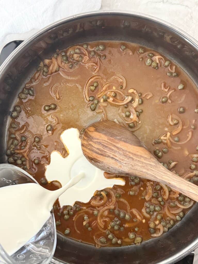 Heavy cream is being added to a large skillet with the base of the smoked salmon pasta sauce.