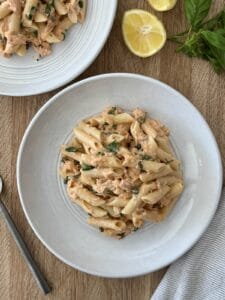 A photo of two white pasta bowls with smoked salmon pasta and fresh lemon slices on the cutting board with fresh basil for garnish and a fork off to the left of the serving bowl.