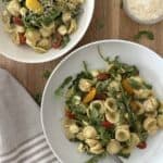 Two bowls of chicken pesto pasta salad. One bowl has a fork and parmesan cheese is in the background.
