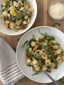 Two bowls of chicken pesto pasta salad. One bowl has a fork and parmesan cheese is in the background.