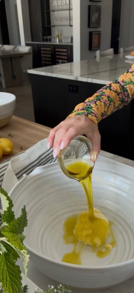 Olive oil is being poured by a hand into a large white bowl with butter in it.