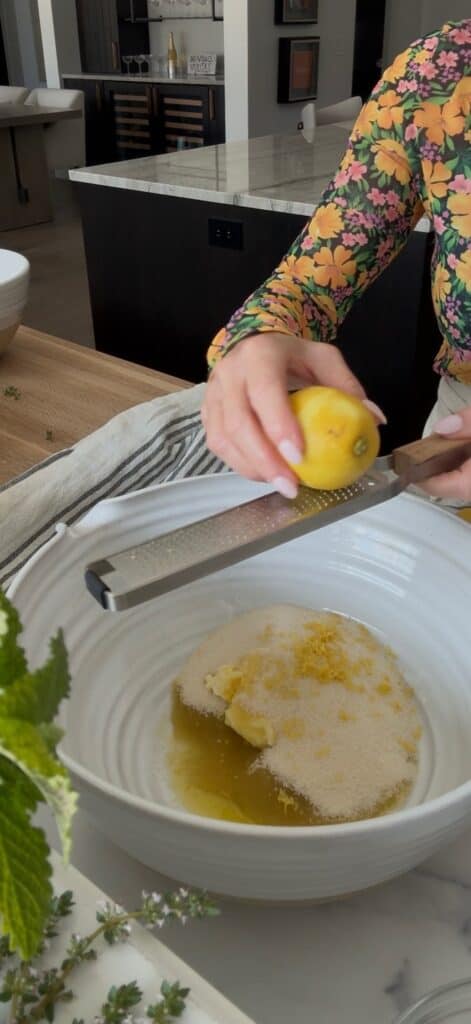 A hand is zesting a lemon on a microplane over the large white bowl of wet ingredients.