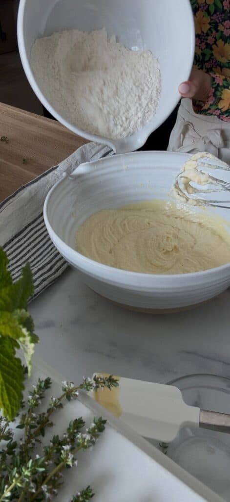 The dry ingredients are in a white bowl and are being added to the wet ingredients in a separate large white bowl.