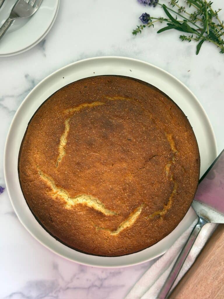 Lemon ricotta cake is baked and on a white plate. The cake is ready to be garnished with powdered sugar.