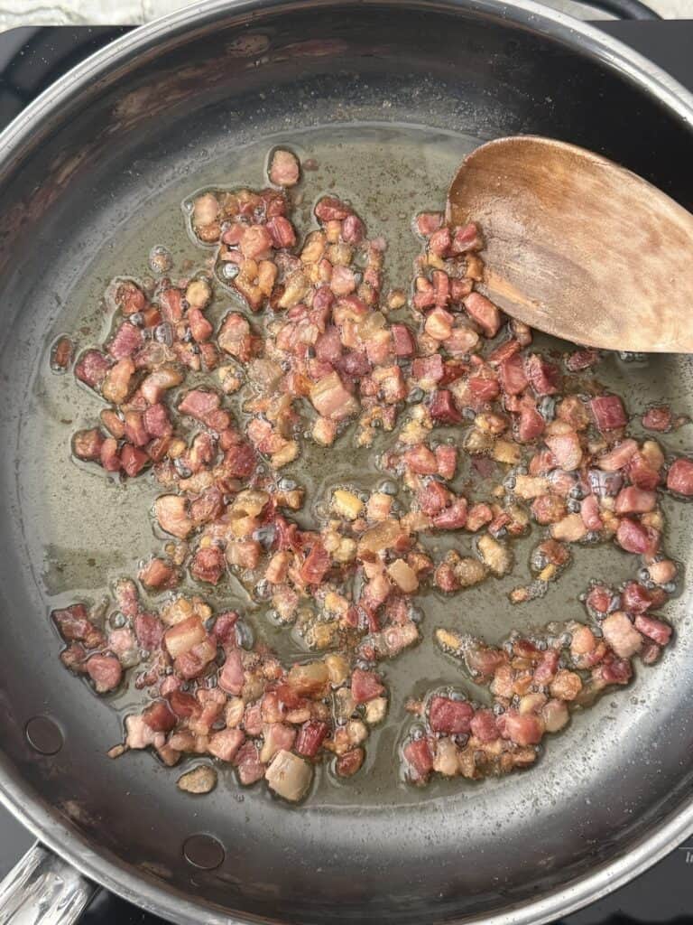 Crisping diced pancetta in a stainless steel skillet with olive oil, stirred with a wooden spoon as the base for pasta e piselli.