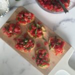 Bruschetta al Pomodoro assembled on a cutting board with chopped tomato, basil, and olive oil.