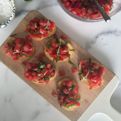 Bruschetta al Pomodoro assembled on a cutting board with chopped tomato, basil, and olive oil.