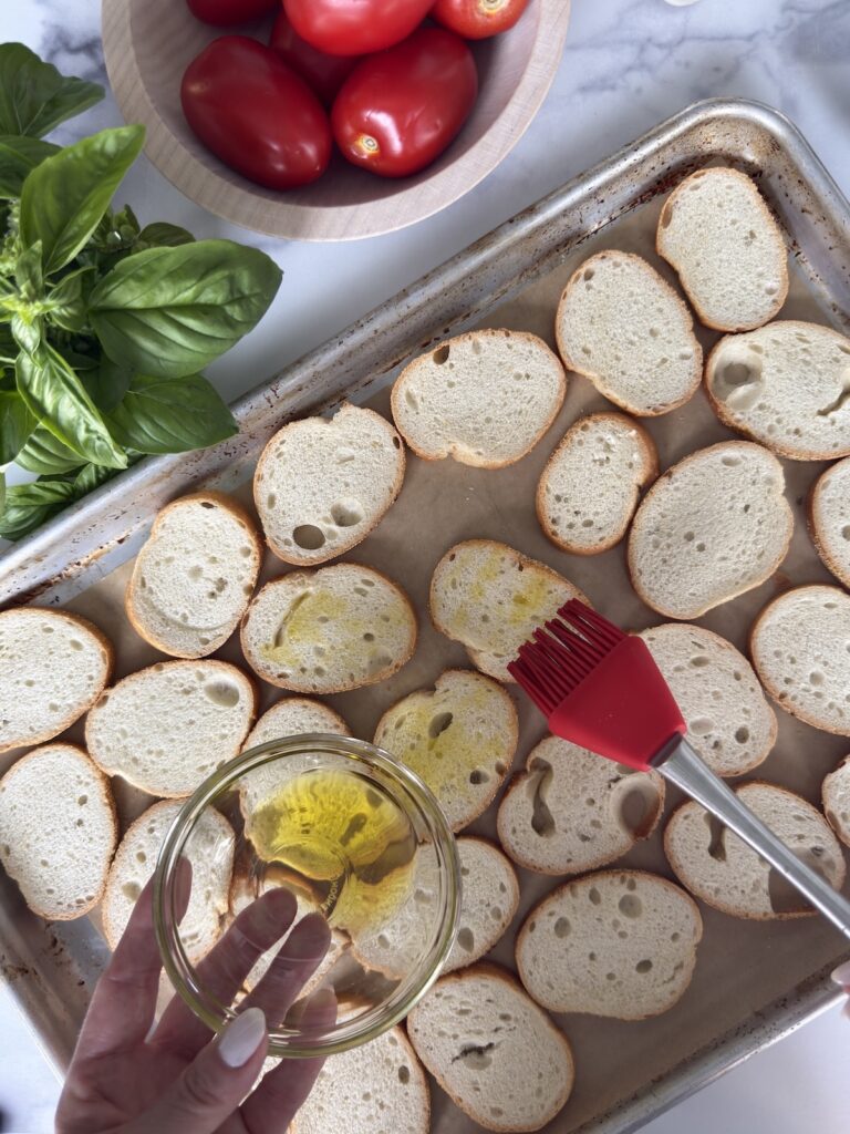 An overhead photo of brushing the baguette slices with olive oil before going into the oven.