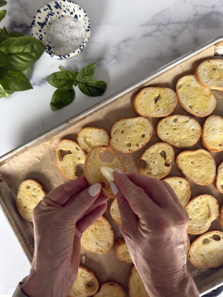 Rubbing toasted baguette slices with fresh garlic for bruschetta al pomodoro.