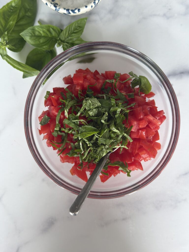 Chopped tomatoes and fresh basil in a glass bowl for Bruschetta al Pomodoro, ready to be mixed.