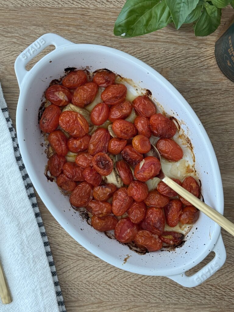 Roasted cherry tomatoes in a white Staub baking dish, caramelized and blistered, used as the base for burrata pasta with roasted tomatoes.