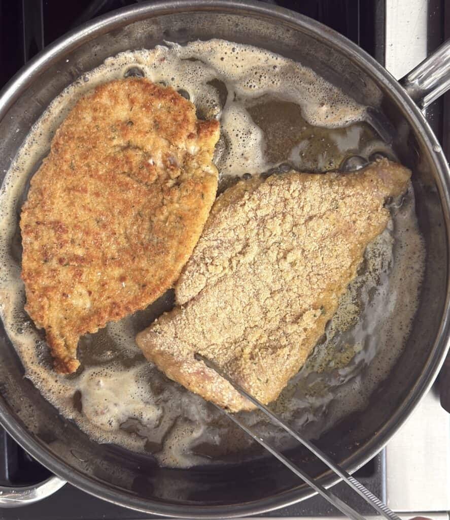 Breaded chicken cutlets frying in hot oil in a stainless steel pan, with visible bubbling around the edges.