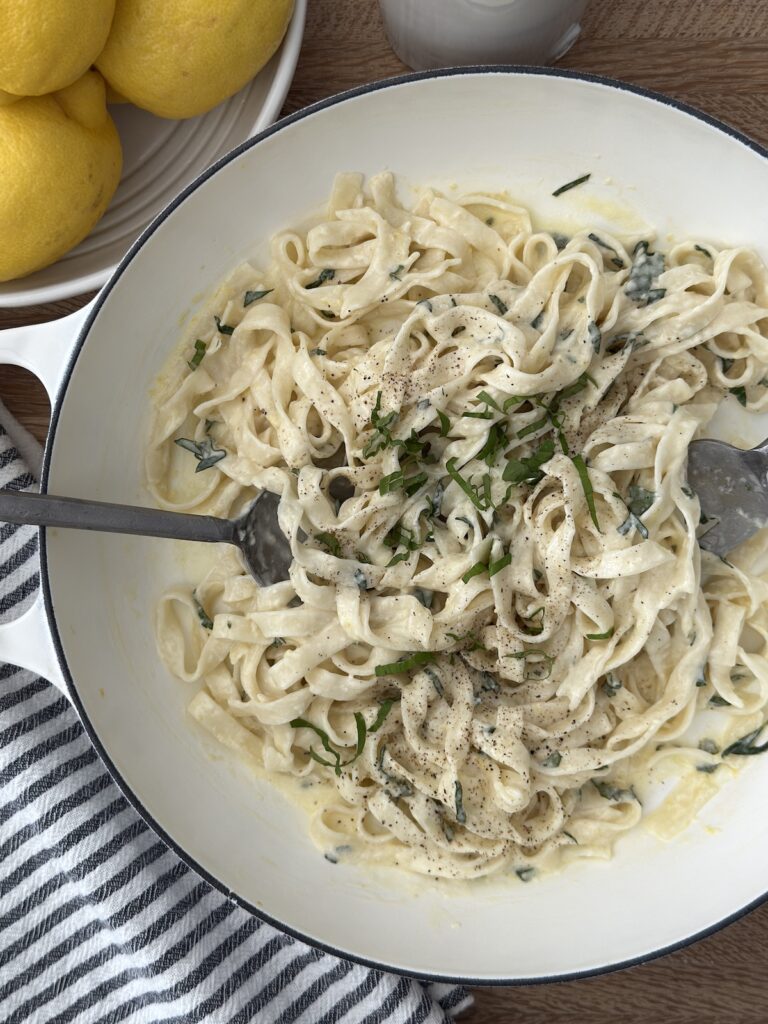 Creamy lemon spaghetti served in a wite bowl with fresh herbs, with a fork and knife twirling the pasta.