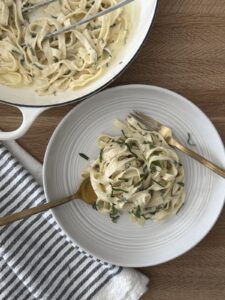 Creamy lemon spaghetti served in a wite bowl with fresh herbs, with a fork and knife twirling the pasta.