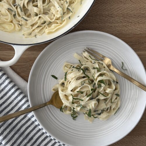 Creamy lemon spaghetti served in a wite bowl with fresh herbs, with a fork and knife twirling the pasta.