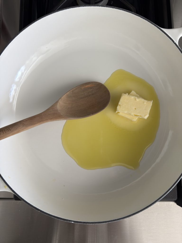 A white skillet with butter, olive oil and a wooden spoon