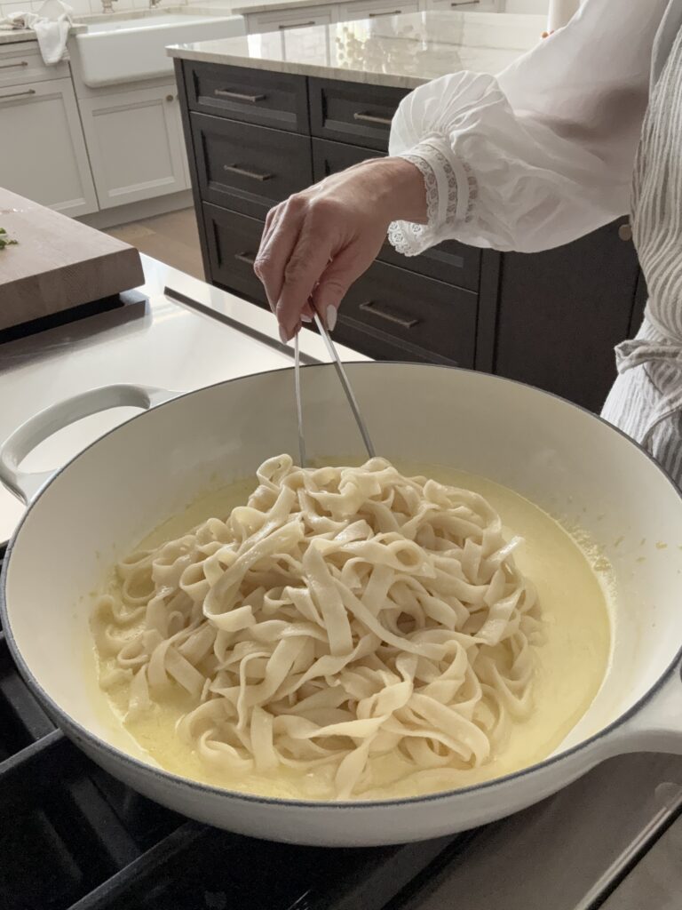 A photo tossing the pasta with the lemon ceam sauce at the stove with tongs.
