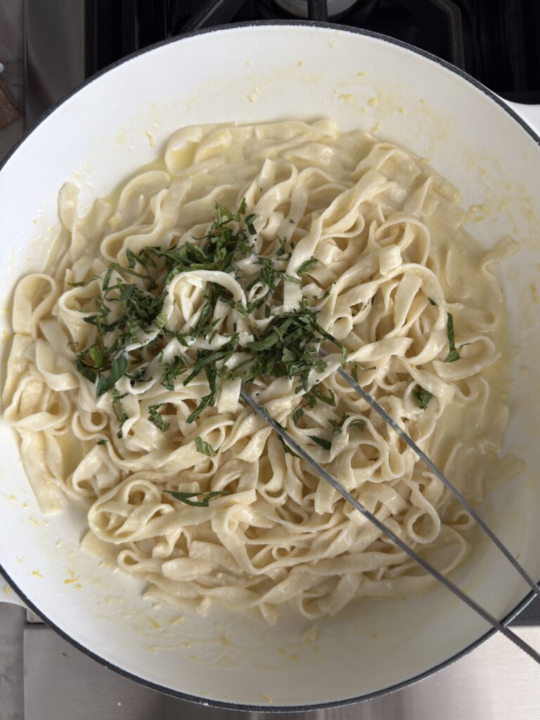 Overhead shot tossing the creamy lemon pasta wth fresh herbs in a white skillet.