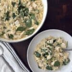 Overhead photo of the Lemon Chicken orzo in a white skillet and a serving bowl with a linen napkin and serving spoons.