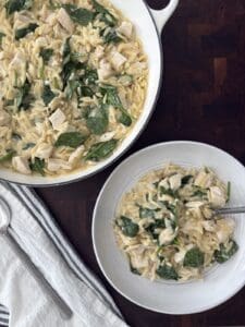 Overhead photo of the Lemon Chicken orzo in a white skillet and a serving bowl with a linen napkin and serving spoons.