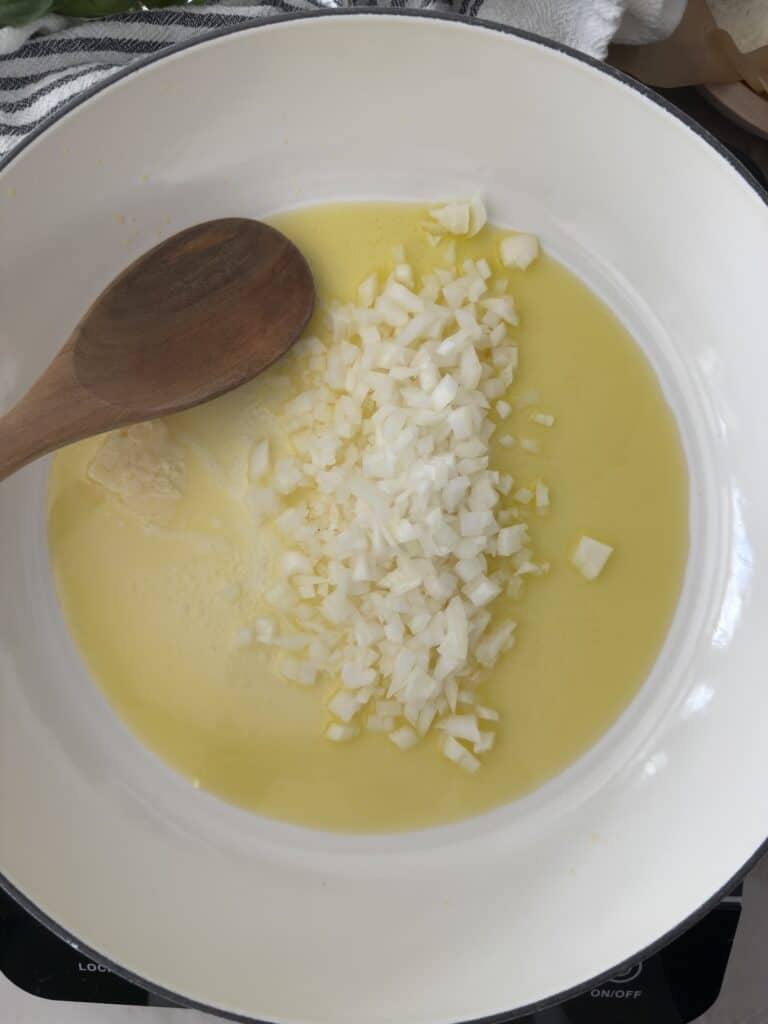 Chopped onion sauteeing in olive oil and butter in a white skillet with a wooden spoon for lemon chicken orzo.