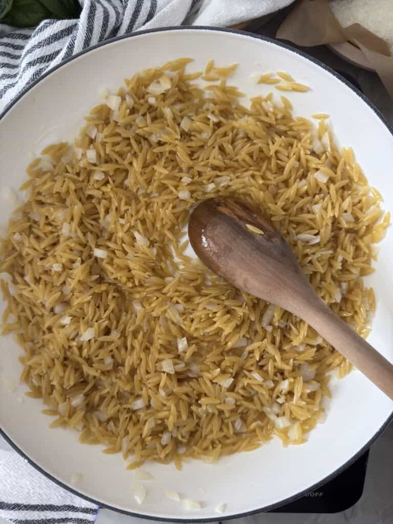 Toasted orzo in the skillet with olive oil, onion and butter. Wooden spoon in the skillet.