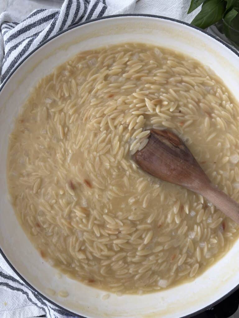 Overhead shot of the orzo cooking in the chicken broth and stirring with a wooden spoon.