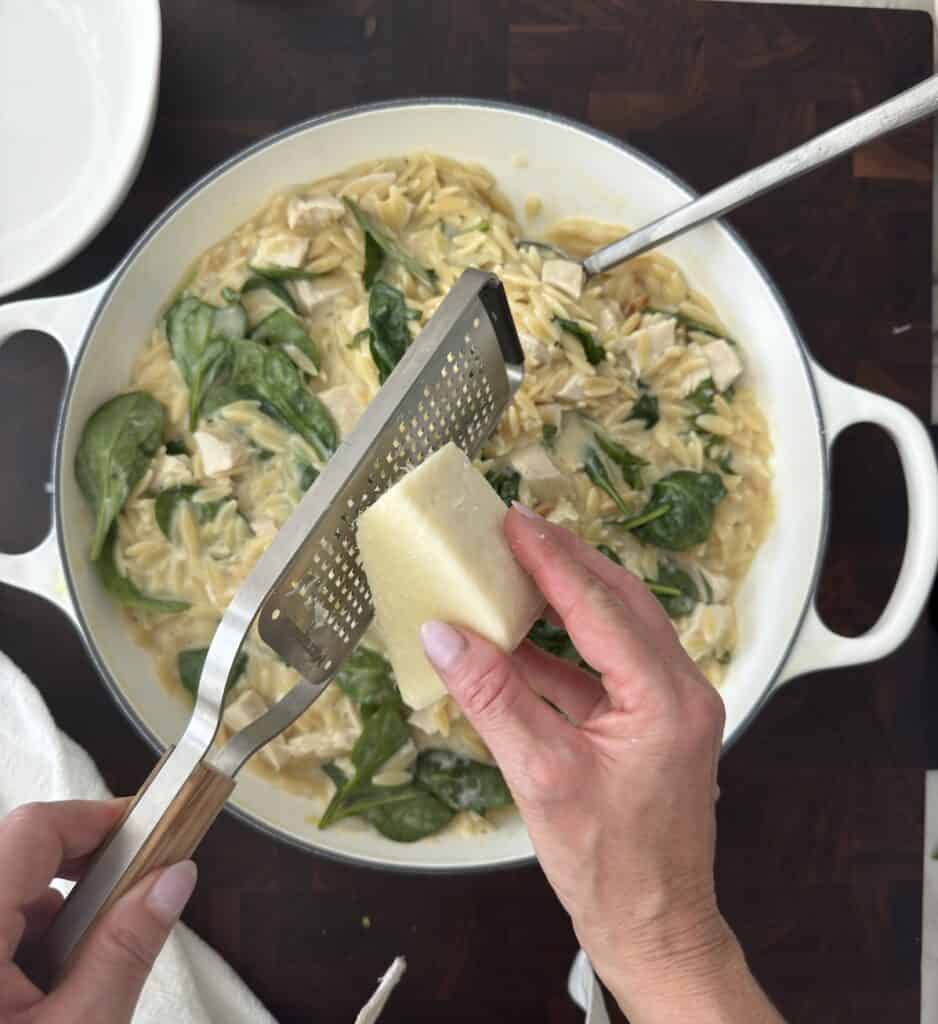 Grating Parmesan cheese over the lemon chicken orzo in a white skillet.