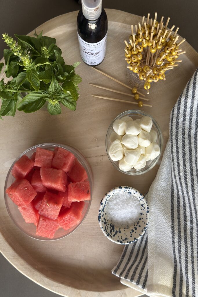 Ingredients for watermelon salad on a wooden tray with Fresh mozzarella, fresh basil, flaky sea salt, and balsamic glaze.