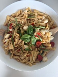 Caprese pasta salad with cherry tomatoes, mozzarella pearls, rotini pasta, and fresh basil leaves tossed with vinaigrette in a white bowl