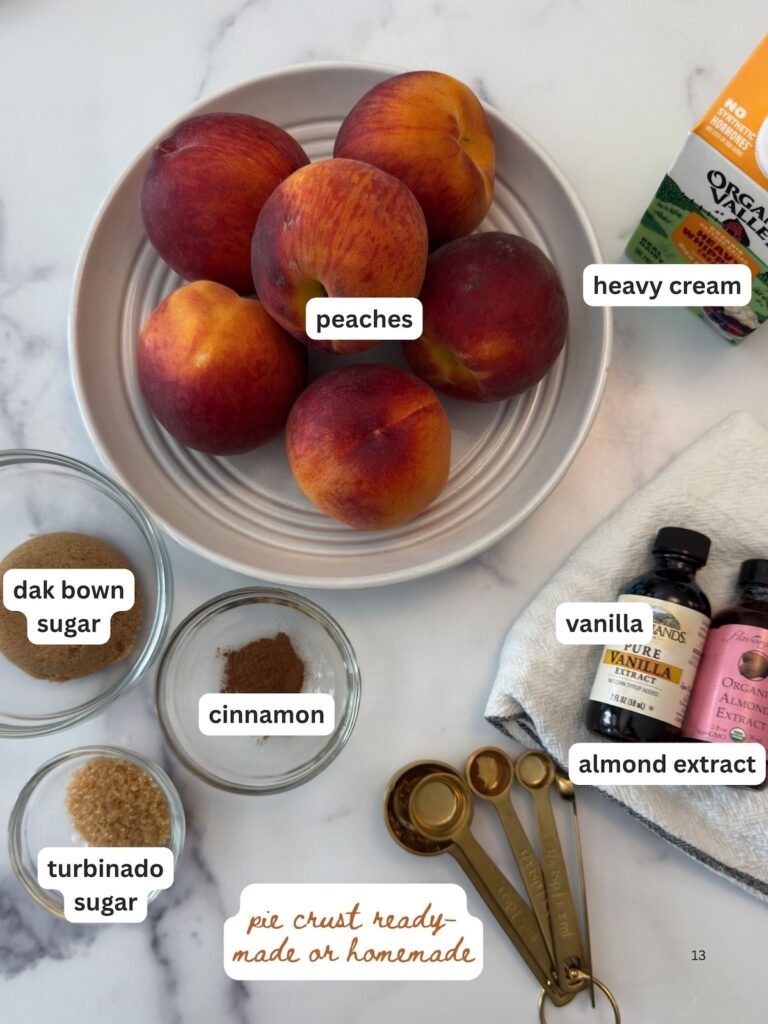 Overhead shot of ingredients for peach crostata recipe, including fresh peaches, brown sugar, almond extract, cinnamon, lemon juice, and store-bought pie crust.