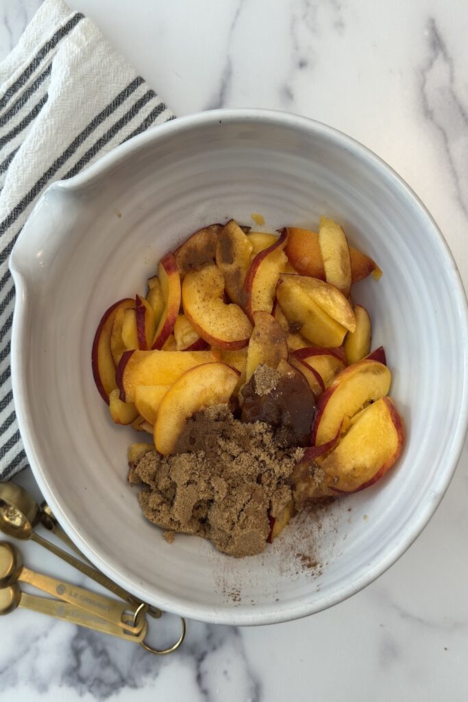 Sliced peaches mixed with brown sugar, cinnamon, and almond extract in bowl for peach crostata filling.