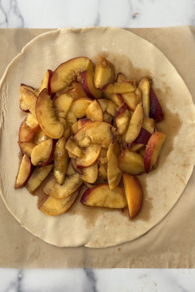 Peach crostata filling with sliced peaches arranged on pie crust before folding and baking.