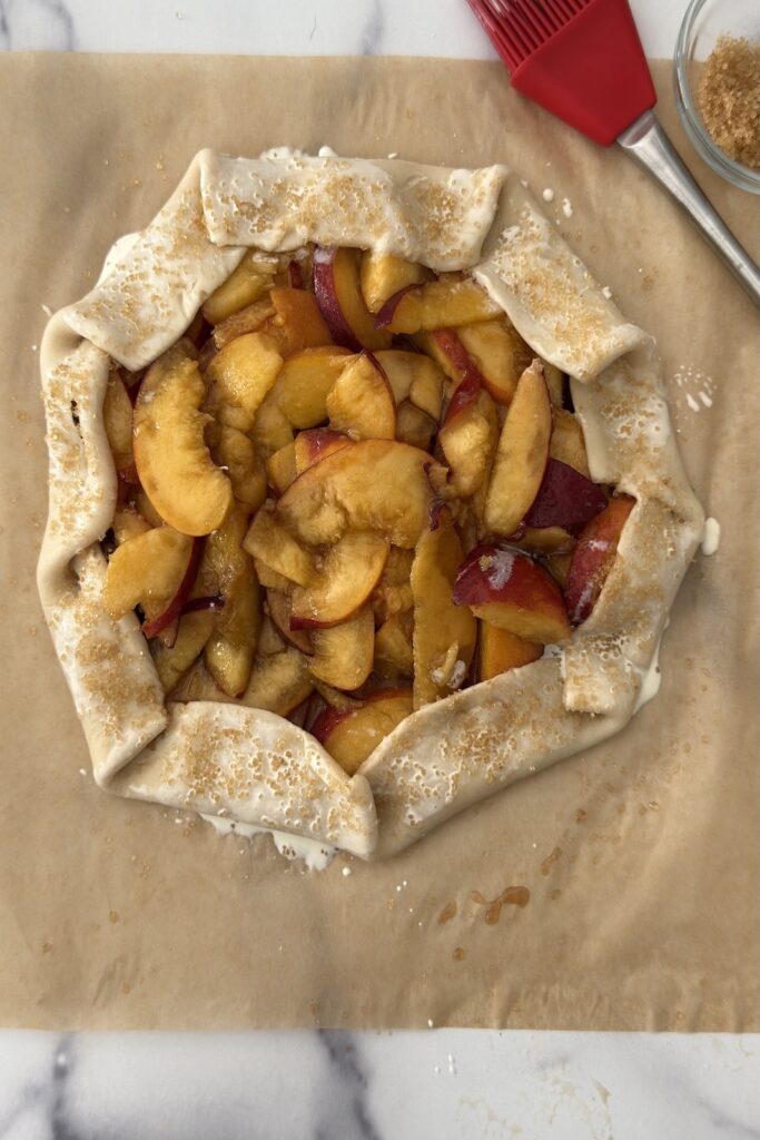 Unbaked peach crostata with folded edges, filled with fresh peaches and ready for the oven.