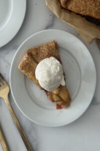 Slice of peach crostata with golden flaky crust, fresh peaches, and a scoop of vanilla gelato on white plate — easy peach crostata recipe for summer dessert.