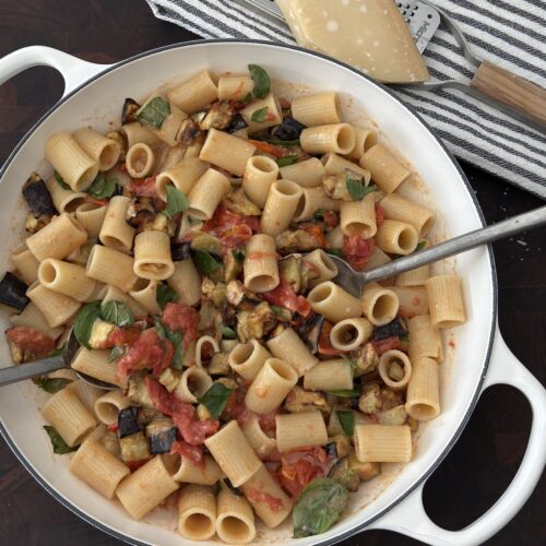Creamy eggplant pasta with rigatoni, roasted cherry tomatoes, mascarpone, and basil in a white skillet topped with Parmesan.
