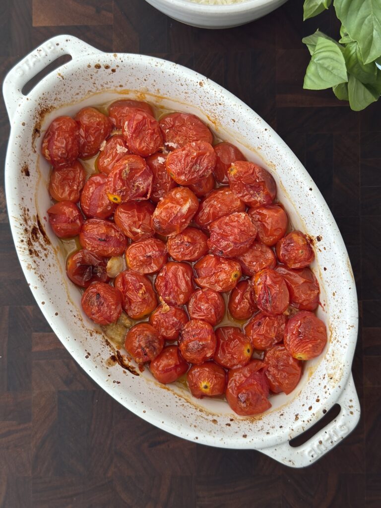 Roasted cherry tomatoes with olive oil in a white baking dish, used for creamy eggplant pasta with mascarpone and basil.