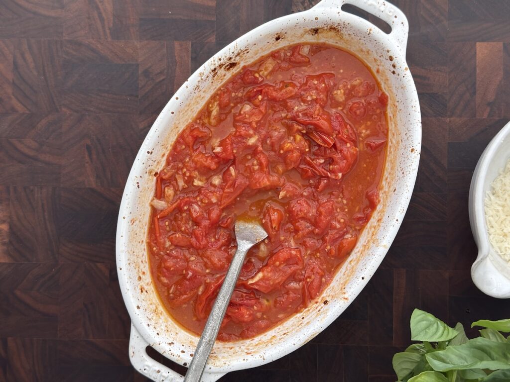 Roasted cherry tomato and garlic sauce smashed into a rich base for creamy eggplant pasta, shown in a white baking dish with basil nearby.