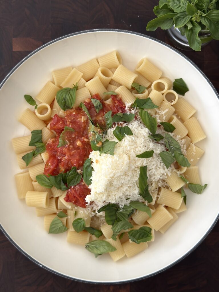 Creamy eggplant pasta served in a white bowl with roasted cherry tomatoes, mascarpone cheese, grated Parmesan, and fresh basil.