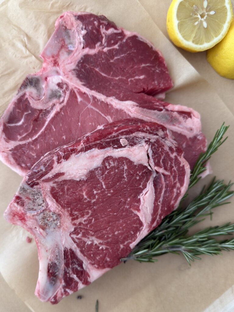 Raw bone-in Italian steaks on parchment paper with fresh rosemary and lemon slices