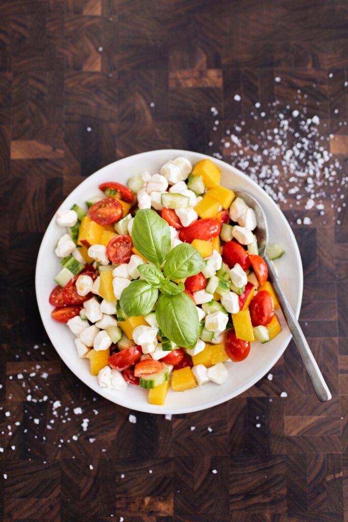 Bowl of peach caprese salad with cherry tomatoes, cucumber, mozzarella pearls, and fresh basil