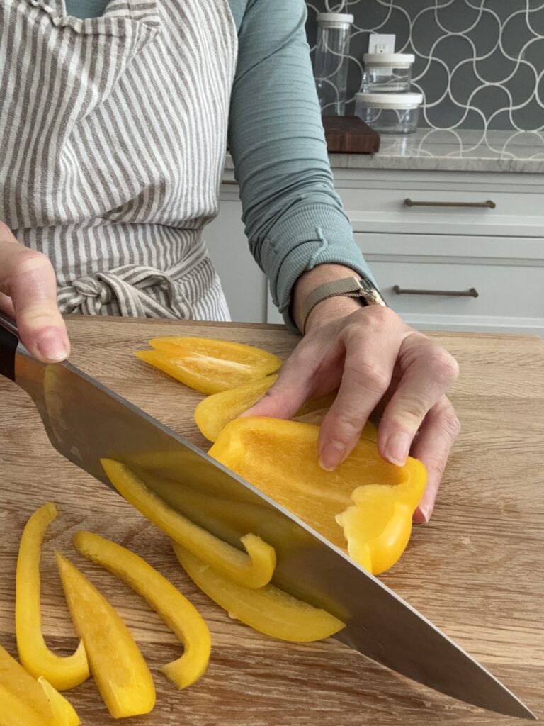 Slicing a yellow bell pepper on a wooden board – prepping vegetables for Italian pepperonata recipe