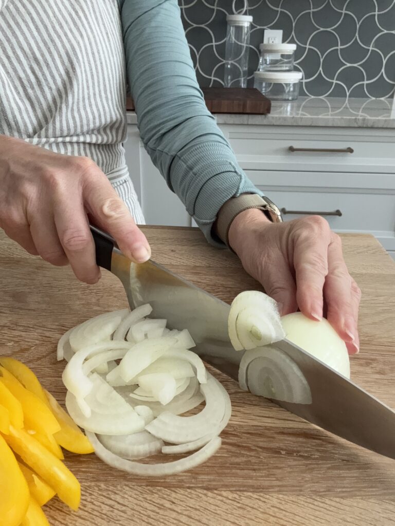 Slicing a white onion on a wooden board for Italian pepperonata – step-by-step cooking process
