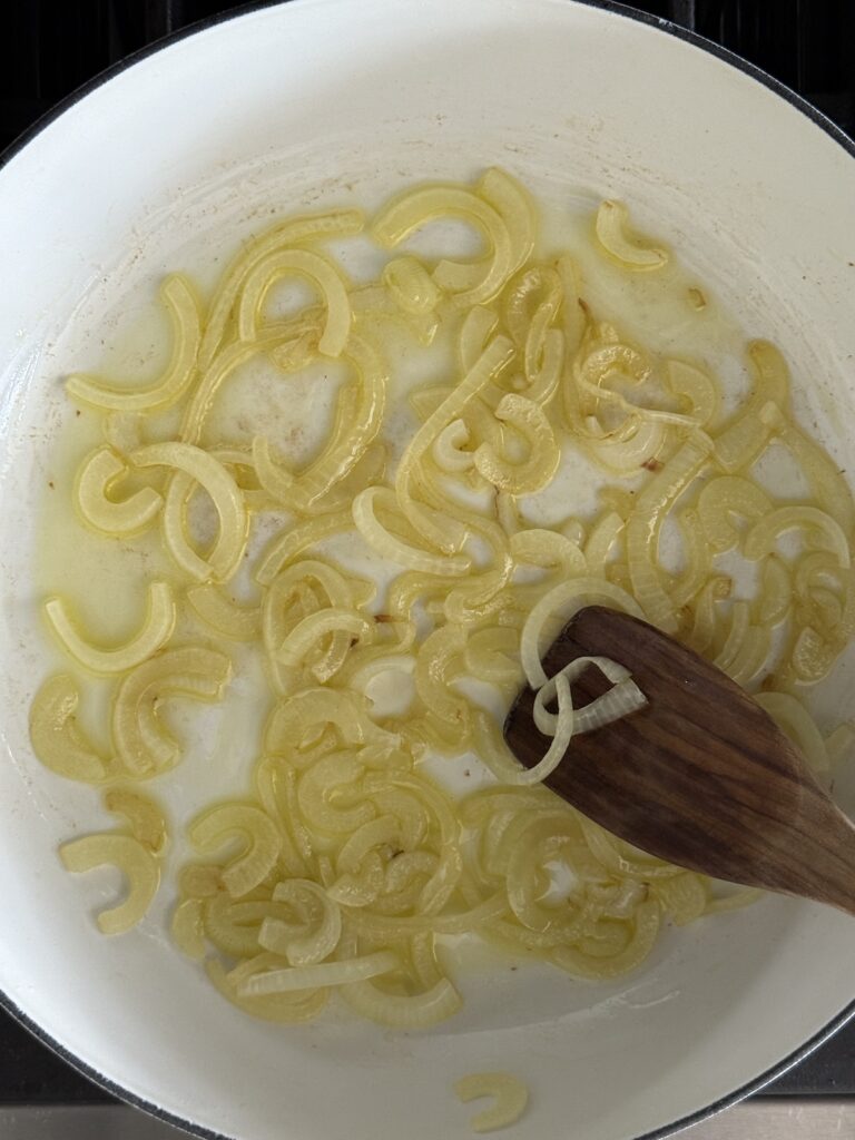 Sautéed onions cooking in olive oil in a white pan – first step of Italian pepperonata recipe