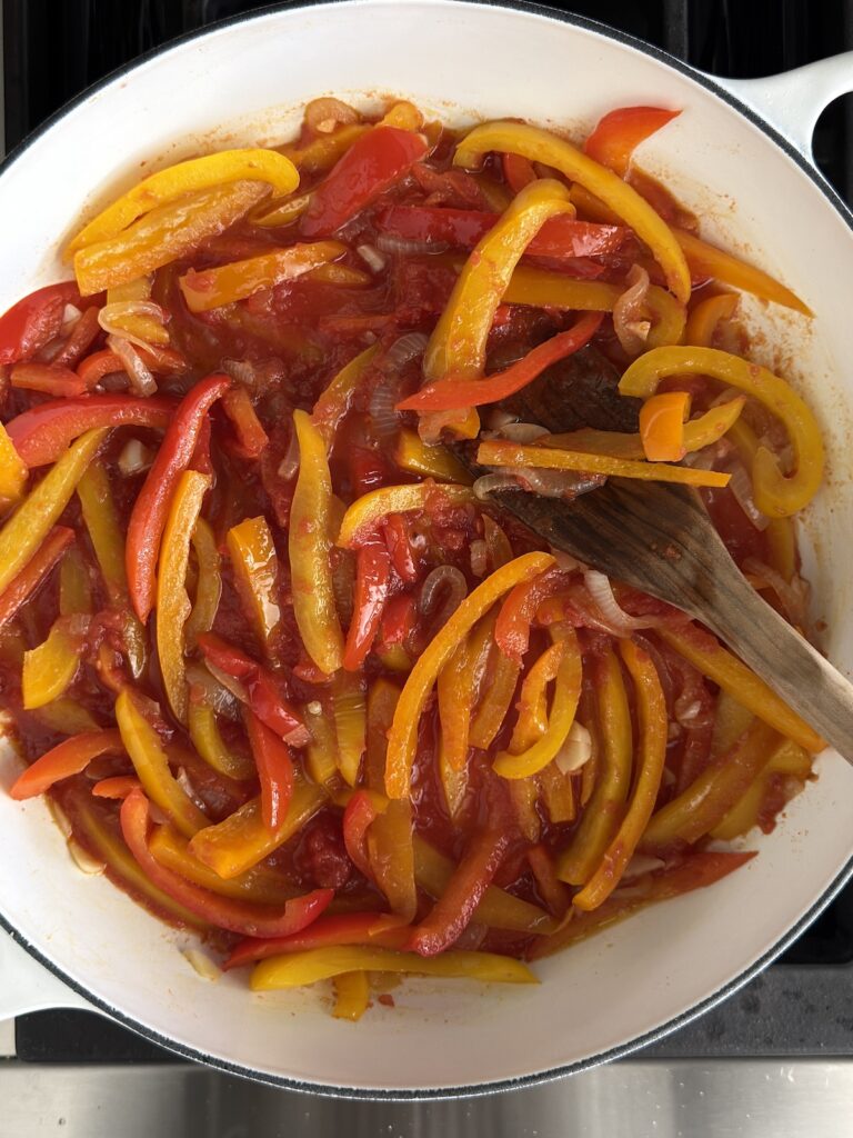 Cooked bell peppers and onions simmering with tomatoes in a white pan – finished Italian pepperonata recipe