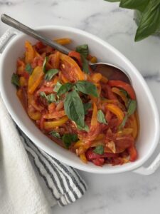 Italian pepperonata served in a white oval dish with fresh basil – sweet peppers and onions simmered with tomato