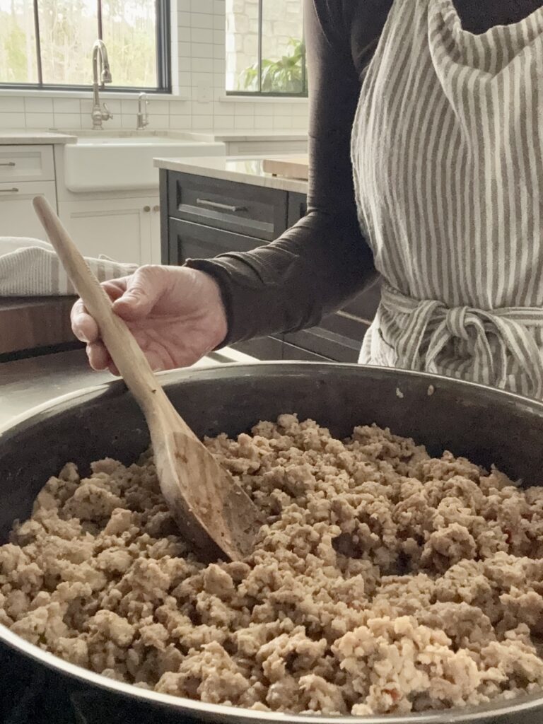 Ground chicken and Italian sausage browning in a stainless steel skillet with a wooden spoon, the first step in making Easy Chicken Bolognese