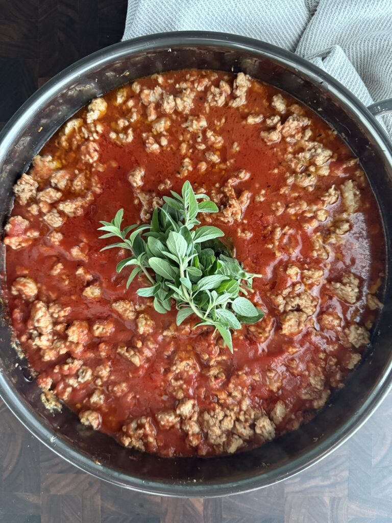 Easy Chicken Bolognese with Italian Sausage simmering in a skillet with tomato sauce and fresh oregano sprigs on top
