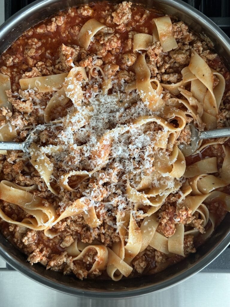 Easy Chicken Bolognese with Italian Sausage tossed with pappardelle pasta in a skillet and topped with grated Parmesan cheese